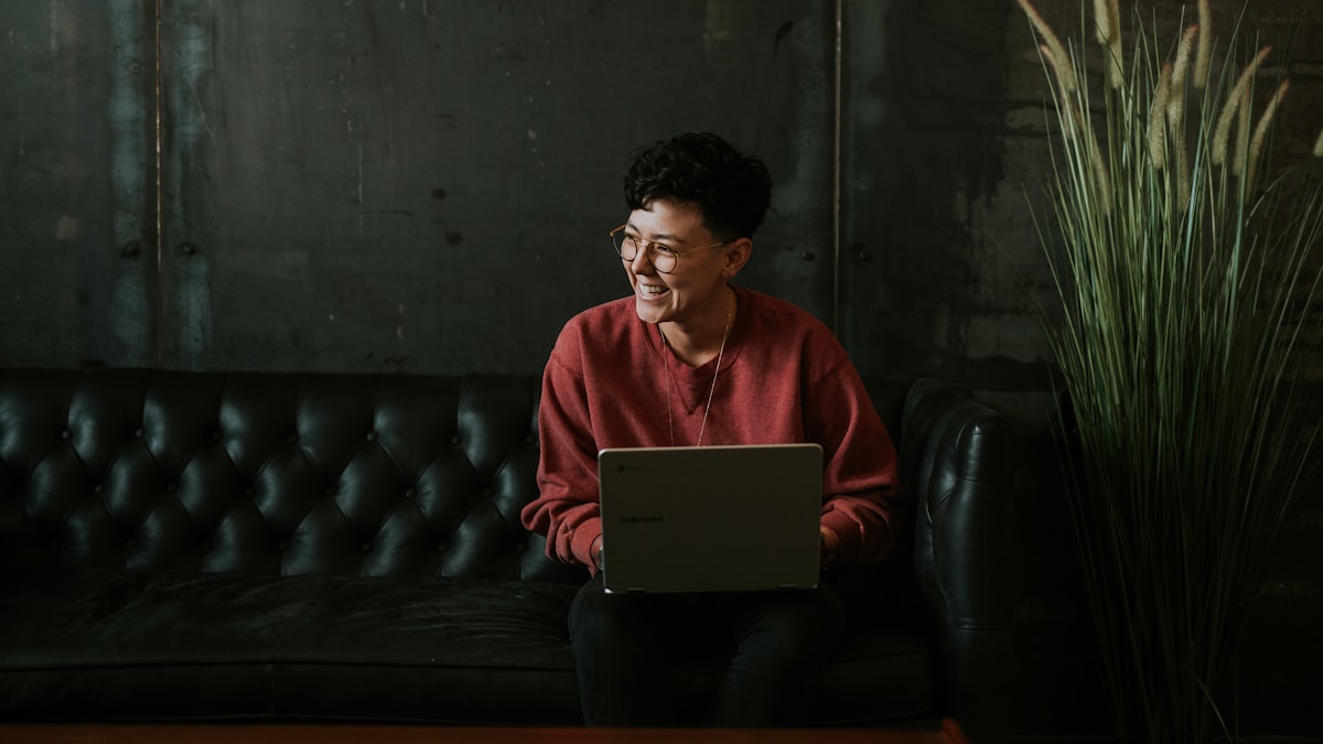 Person mit Brille sitzt auf einem Sofa mit Laptop und lacht — Symbolbild zu einem Beitrag.