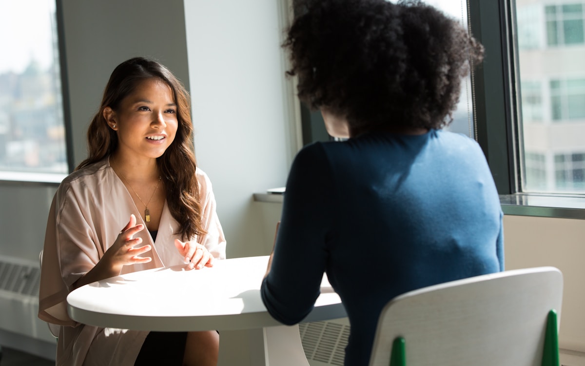Zwei junge Frauen sitzen am Bistrotisch im hellen Büro im Gespräch.